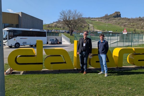 Zwei Männer stehen nebeneinander vor einem großen Schriftzug „dallara“ auf einer Wiese