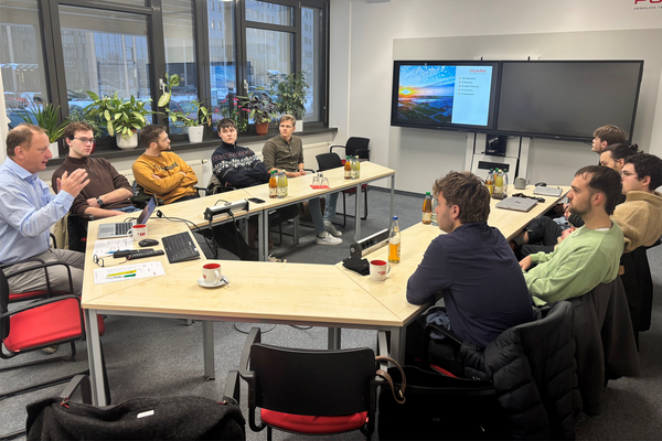 Teilnehmenden sitzen um runden Tisch und hören Vortrag