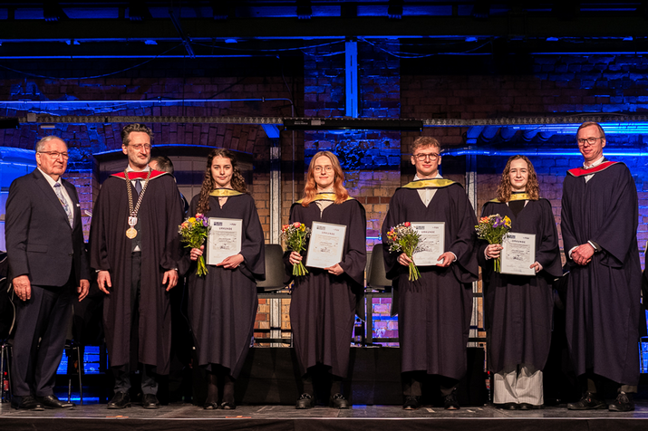 Gruppenfoto auf der Bühne, die Preisträgerinnen und Preisträger halten Urkunde und Blumen in der Hand