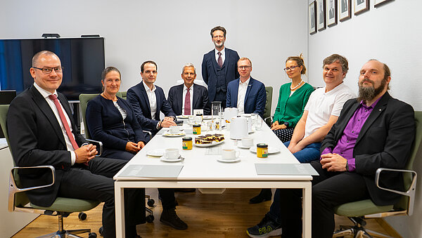 Neuberufene Profs. Okt. 2025 mehrere Personen sitzen als Gruppe an einem Tisch und lächeln in die Kamera