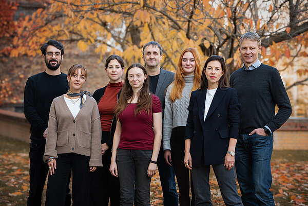 8 Personen stehen für ein Gruppenbild auf einer herbstlichen Wiese