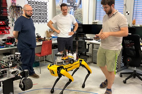 Labor, drei Männer stehen um einen gelben Roboter, mit vier Beinen, wie ein Roboterhund