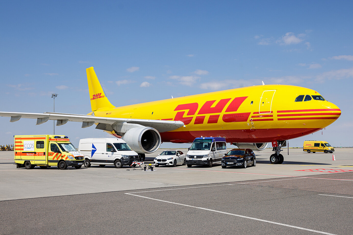 Rettungswagen, Transporter, Roboter-Hunde und ein DHL-Flugzeug stehen auf der Rollbahn