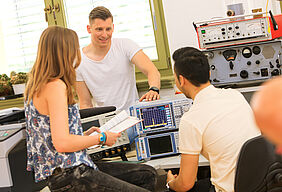 zwei Studenten und eine Studentin in einem Labor am Arbeitstisch (mit Messgerät)