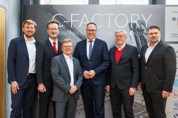 C-Factory Sechs Männer vor breitem RollUp mit Aufschrift C-Factory