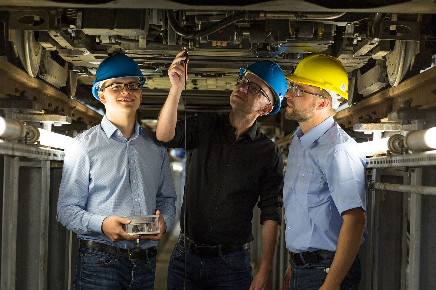 Maik Wolf, Professor Mathias Rudolph und Robert Richter vom LVB-Tochterunternehmen IFTEC stehen in einer Straßenbahnwartungsgrube und testen das entwickelte System.