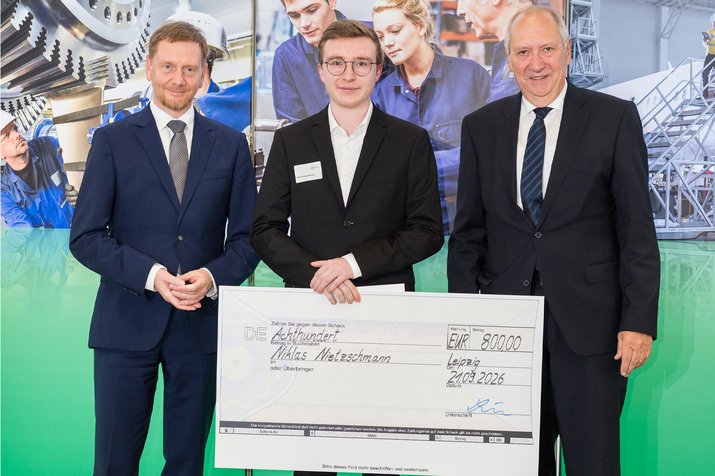 Group photo; the award winner in the center is holding a giant check in both hands