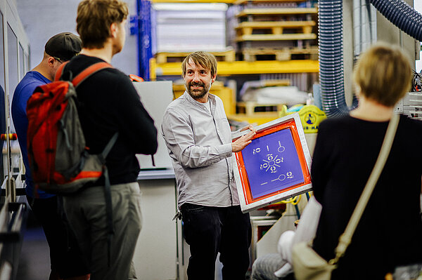 Prof. Ingo Reinhold Tag der offenen Tür Ein Mann zeigt einer Gruppe ein Bild in einem Rahmen