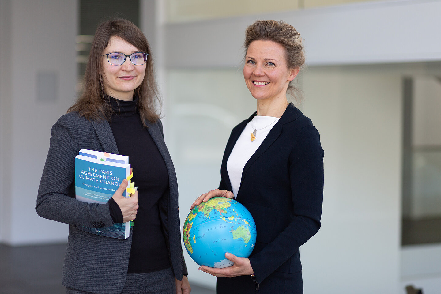 Cornelia Manger-Nestler und Ulrike Will Zwei Frauen mit Büchern und einem Globus in der Händen lächeln in die Kamera.