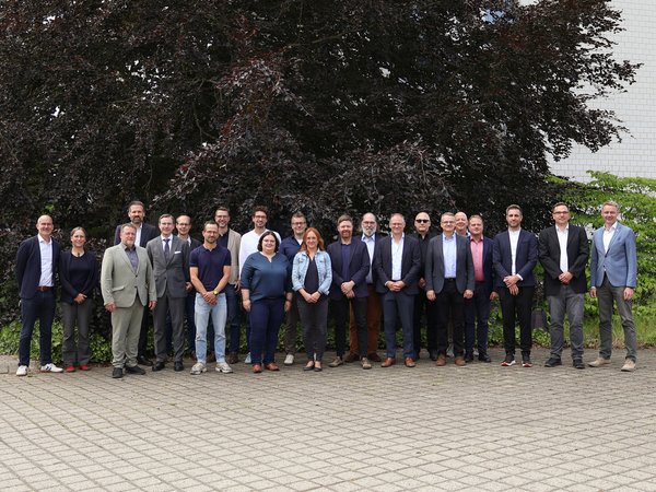 30 Personen stehen im Freien für ein Gruppenbild nebeneinander
