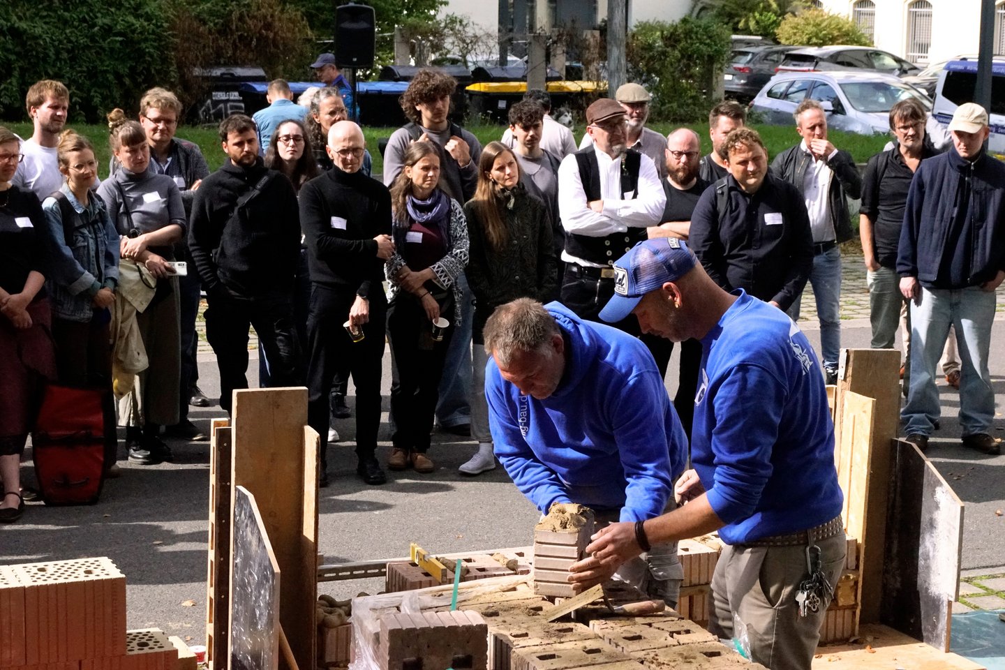 Nachhaltig Bauen und Sanieren 2026 zwei Männer bauen eine Wand, viele Menschen schauen zu