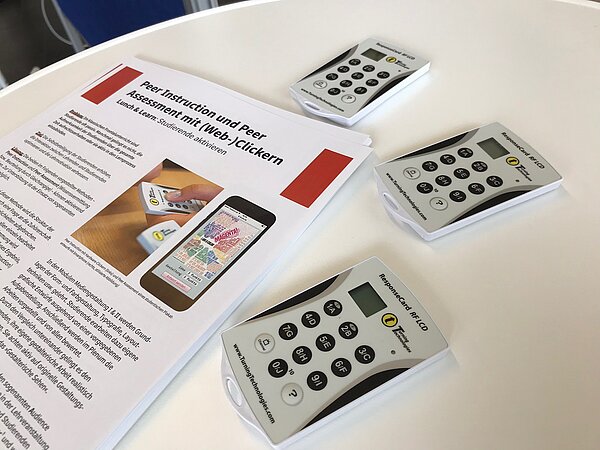Drei digitale Abstimmungsgeräte (optisch ähnlich Taschenrechnern) und Benutzungshinweise auf einem Tisch.