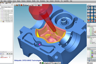 Monitor screen showing CNC programming: red nozzle and blue workpiece visible in a 3D animation