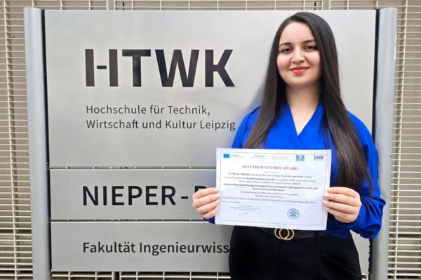 eine Frau steht vor dem Schild des Nieper-Baus der HTWK Leipzig und hält einen Zettel in der Hand