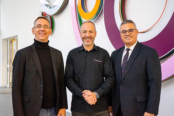 drei Herren im anzug vor einem Kunsterk lachen in die Kamera