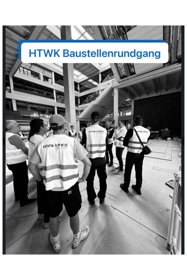 Einige Personen in Warnwesten stehen unter einer Dachkonstruktion, schwarz weiß Foto