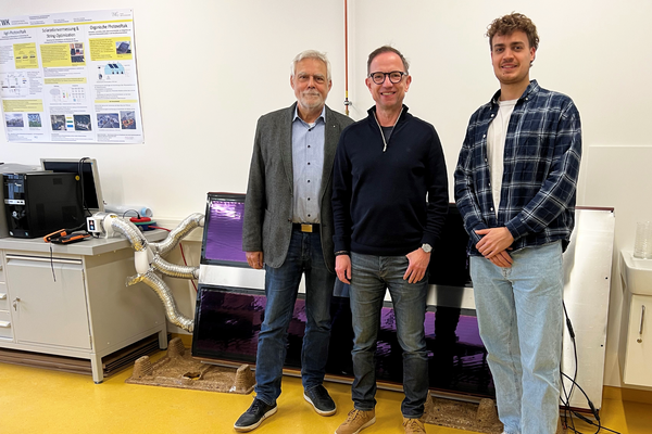 Gruppenfoto der drei Personen, im Hintergrund liegt PVT Modul mit lilafarbener Beschichtung