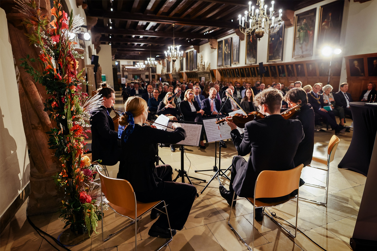 Foto vom Festsaal mit Publikum in Sitzreihen im Vordergrund HTWK Orchester
