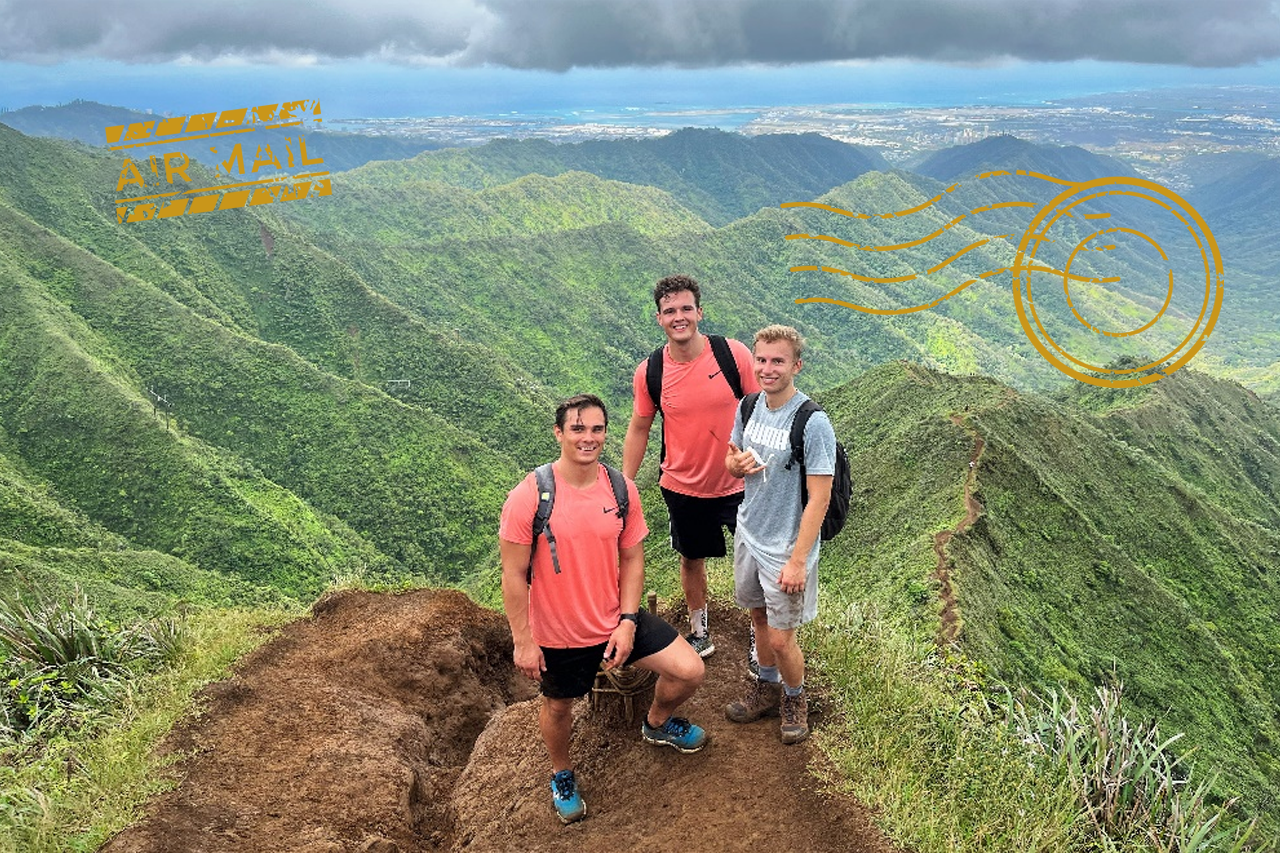 Foto: Drei Studenten schauen in Kamera auf dem Gipfel eines Berges auf Hawaii mit Blick nach Honolulu