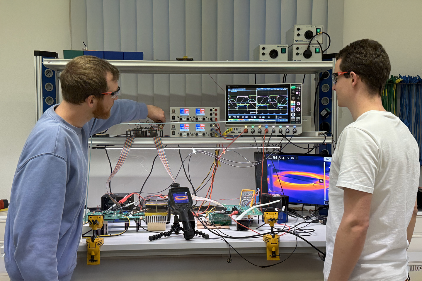 Two employees in the laboratory stand in front of monitors displaying diagrams in different colors.