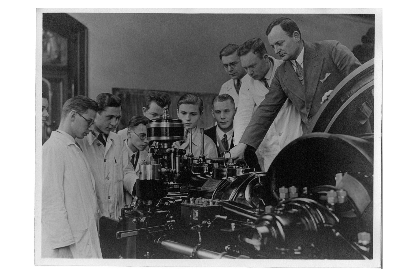 Students in white coats and lecturer standing around machine