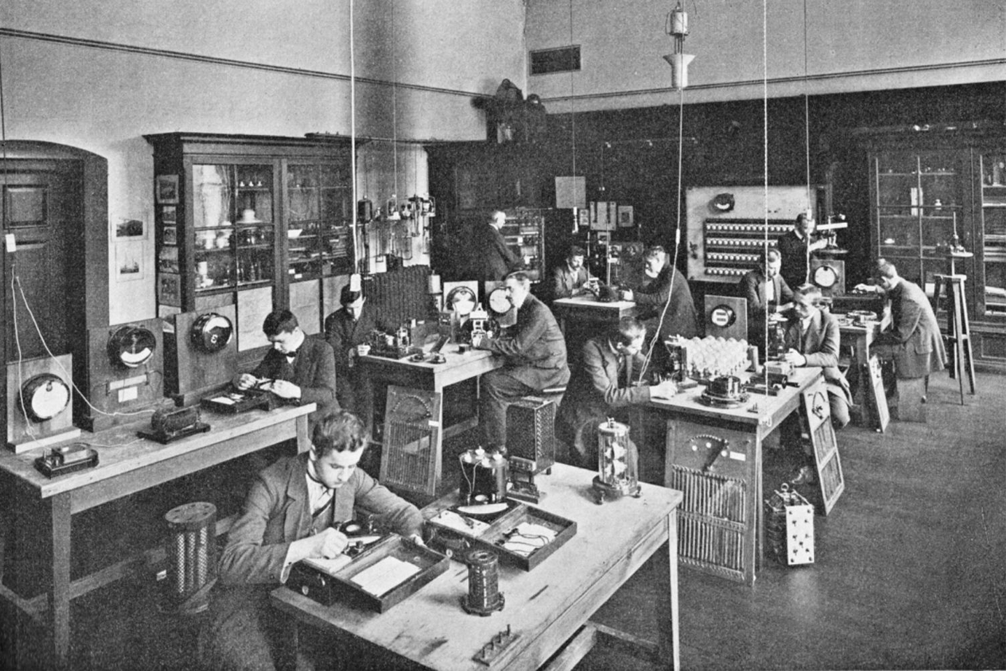 Black and white photograph of the electrical engineering lab Students sitting at small machines on tables