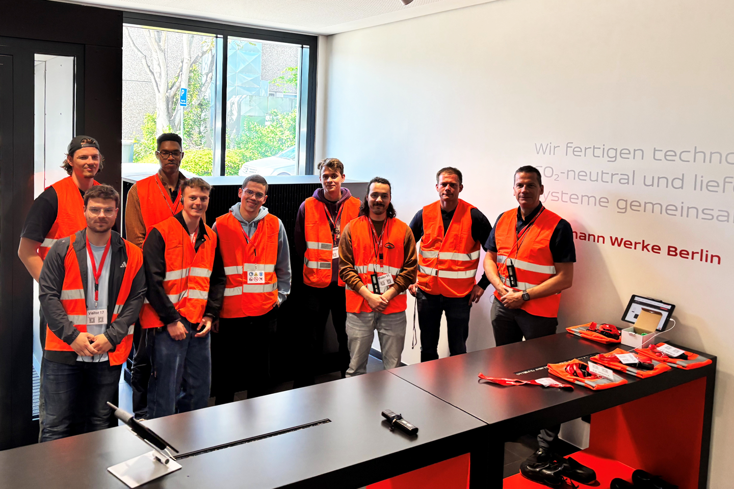 Gruppenfoto in rot-orange leuchtenden Warnwesten in einem großen Büro