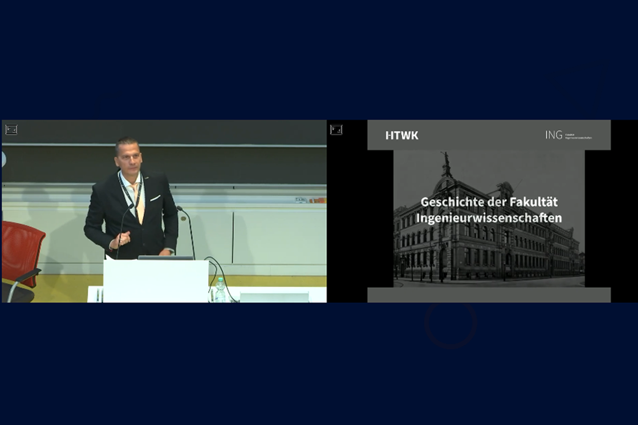 Foto von Präsentation im Hörsaal, links Prof. Guzek, daneben Bild vom Wiener-Bau/Link führt zum Video