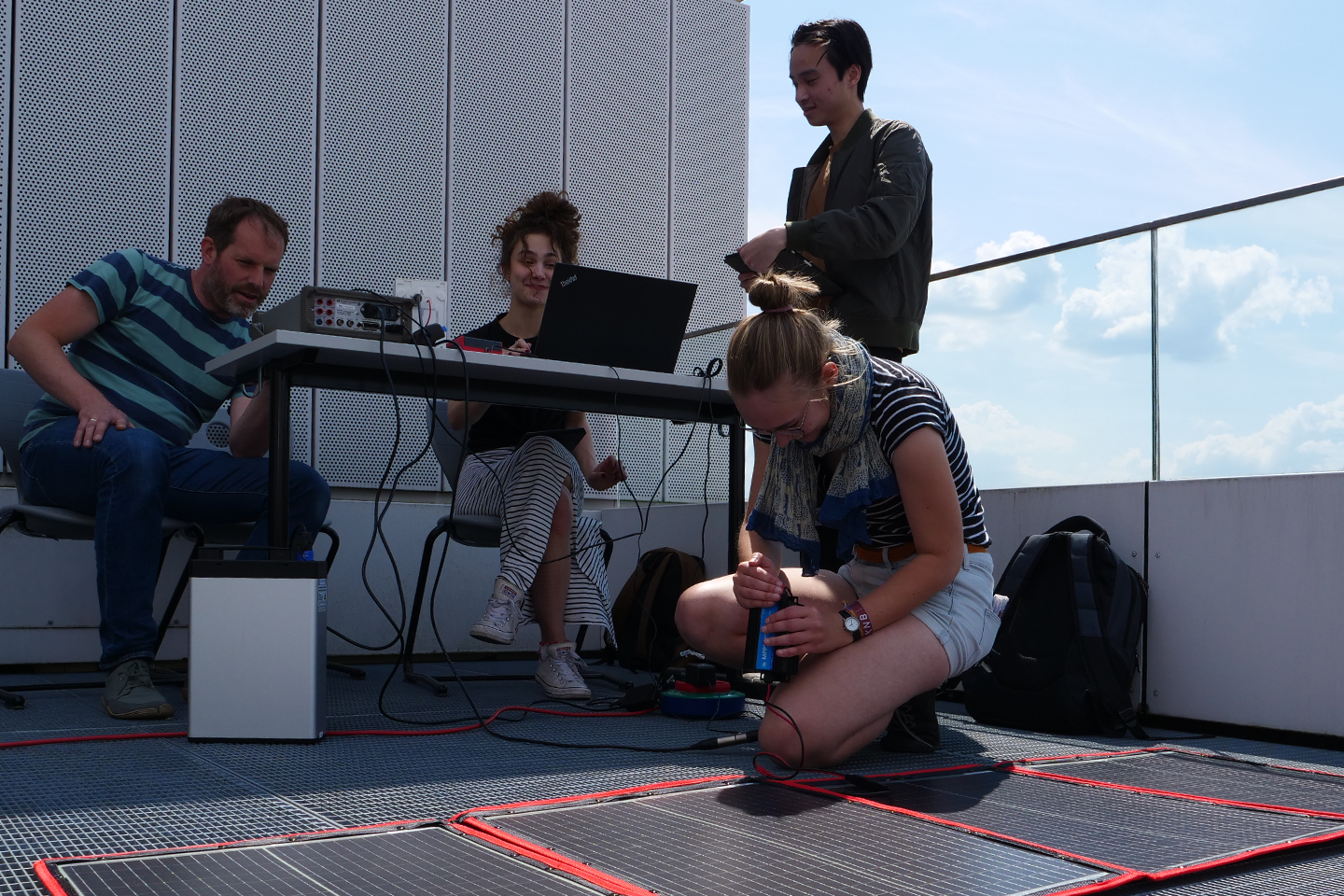 Students are sitting at a table in front of a photovoltaic film and taking measurements/Link leads to the project website