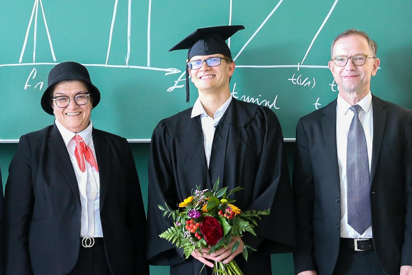 Group photo: Ph.D. candidate Maik Wolf in the center, wearing a gown and mortarboard and holding a bouquet of flowers
