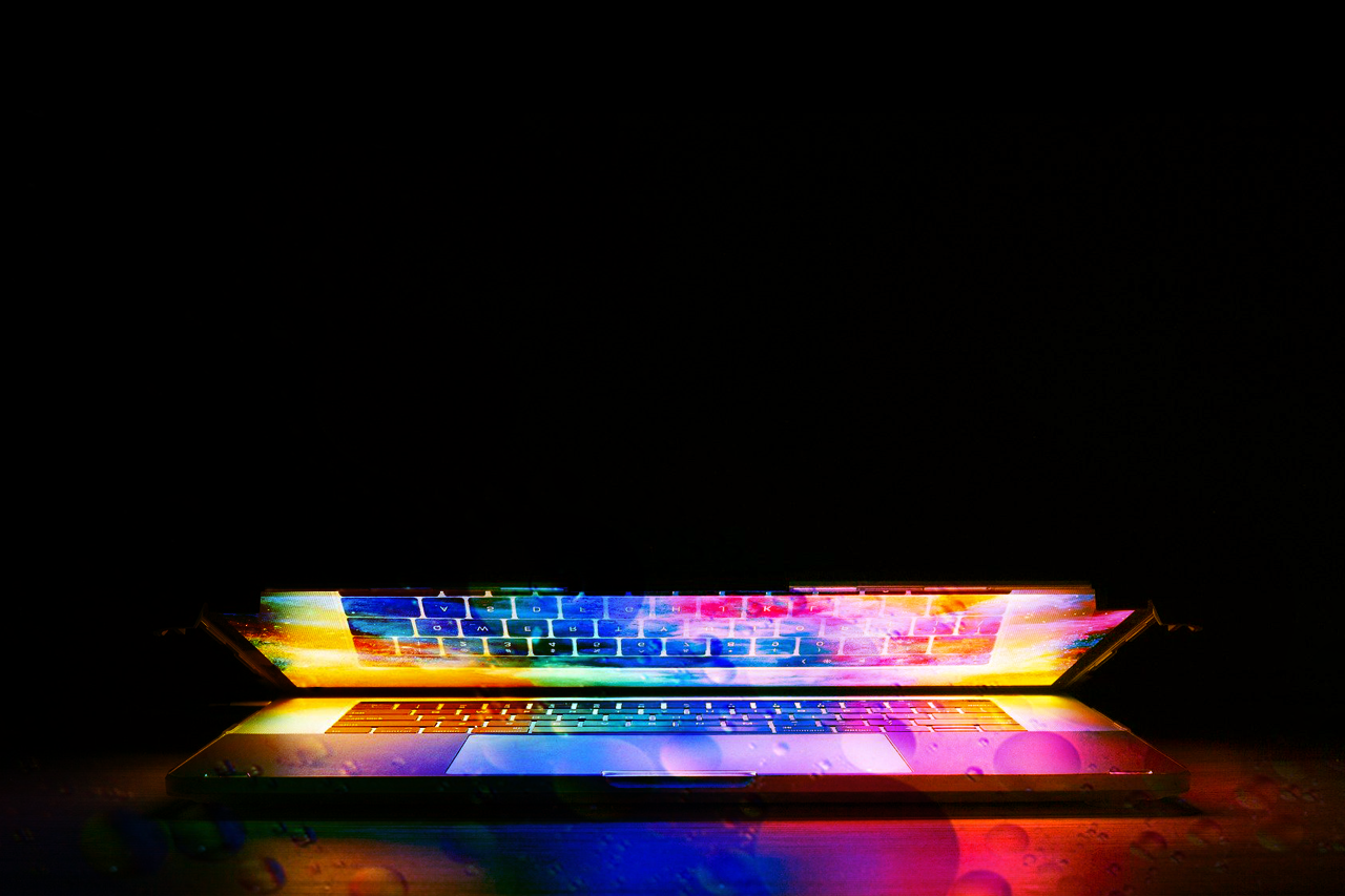 Black background, a laptop glowing in rainbow colors and almost closed / link leads to the project website