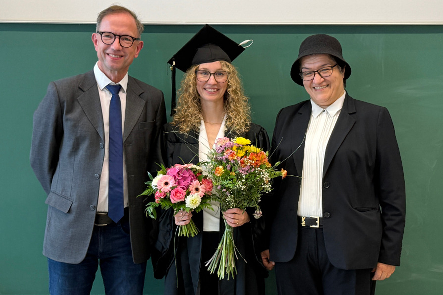 Gruppenfoto, Promovendin hat Blumenstrauß in der Hand und trägt Talar sowie Hut